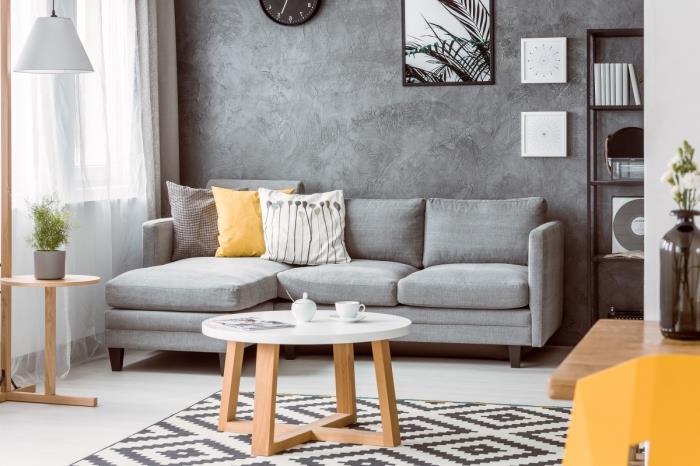minimalistické usporiadanie obývačky s betónovými textúrami, dreveným nábytkom a sivou rohovou sedačkou, bielo -čiernym škandinávskym kobercom
