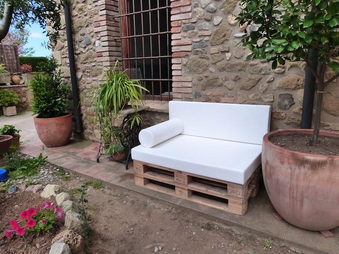 príklad drevenej paletovej stoličky s bielym vankúšom a niekoľkými zelenými rastlinami v záhrade