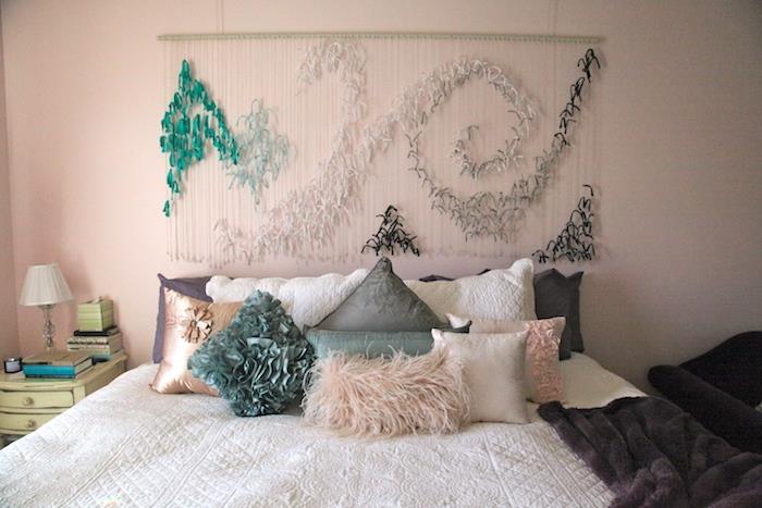sänggaveldekoration i grönt, vitt, svarta fjädrar på vita trådar, kuddar i grönt, grått och rosa, vita sängkläder