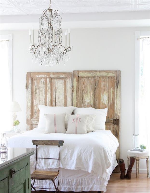 sänggavel med gamla ladugårdar, vita sängkläder, elegant barockkrona, ljus parkett, eleganta lantliga möbler