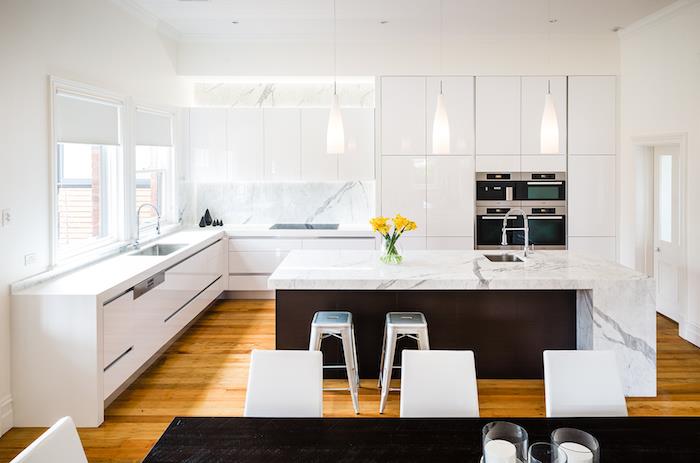 Modernt backsplash i marmor, vita köksmöbler, designerupphängningar, ljus parkett, marmor och svart köksö