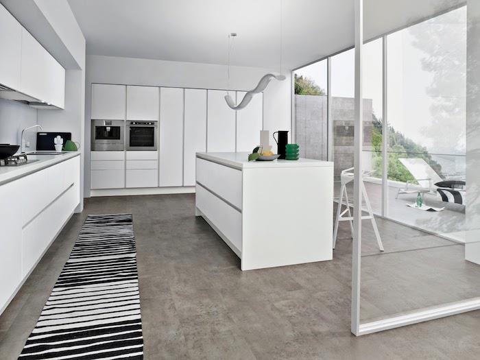 utrustat kök med köksskåp och vit centralö, grått klinkergolv, svartvit matta, rostfria vitvaror, vitt glastak