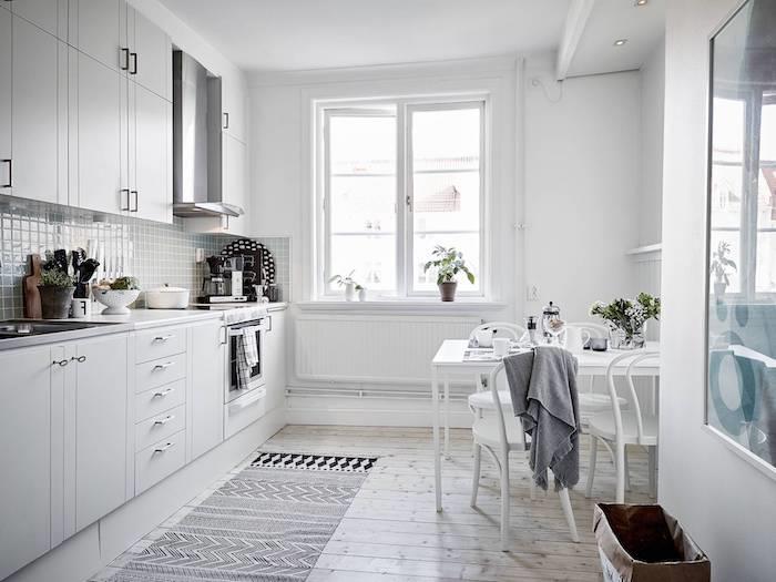 vitt utrustat kök med ljus träparkett, vita köksmöbler, vita bord och stolar i skandinavisk stil, svartvitt matta, vattengrönt stänk