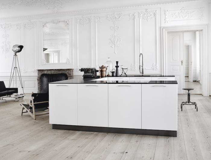 vitt utrustat kök med vit centralö, med svart bänkskiva, väggar dekorerade med vita lister, vintage barock spis, ljus träparkett