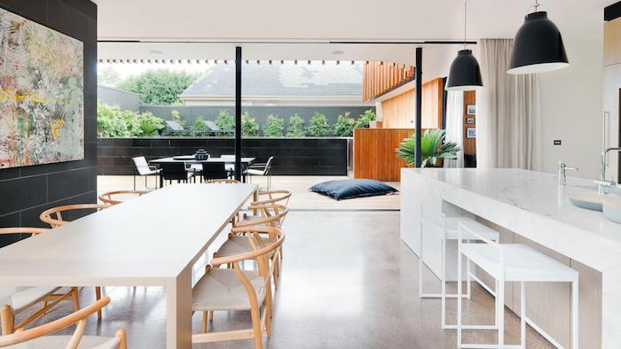 ako zariadiť dlhú bielu kuchyňu s centrálnym ostrovom s mramorovým efektom, jedáleň s dreveným stolom a stoličkami, priemyselné sivé závesné svetlá