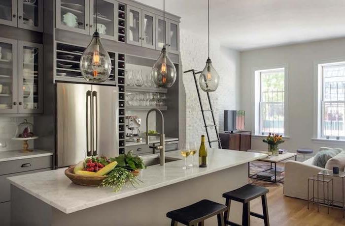 kuchyňa so sivou lištou a mramorovou pracovnou doskou, sivá kuchynská linka, spotrebiče z nehrdzavejúcej ocele, originálne závesné svetlá, biela sedačka, drevený a kovový stôl