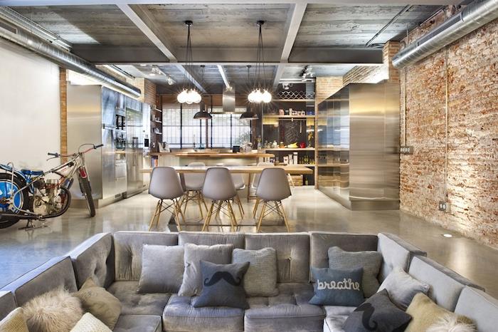 americká kuchyňa v priemyselnom štýle, sivá a drevená kuchyňa otvorená do jedálne, škandinávske stoličky a drevený stôl, sivá rohová sedačka, tehlová stena