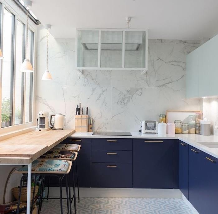 نموذج مطبخ زاوية مع خزانة قاعدة باللون الأزرق الداكن وسطح عمل أبيض ، وغطاء مطبخ وجدار رخامي ، وبار صغير مع مقاعد سوداء ، ومغطى بوسائد ملونة