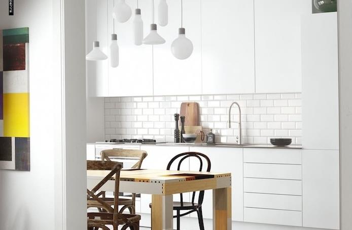 exempel på ett vitlackerat kök med vitt kaklat stänk och vita höga och låga möbler, vita vita hänglampor, träbord och trästolar
