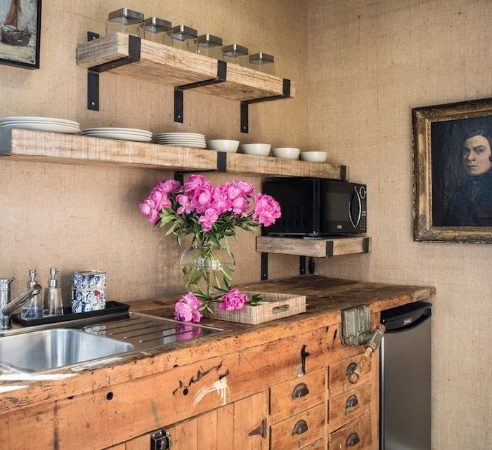 مثال لمطبخ ريفي باللون البيج مع خزانة مطبخ من الخشب الخام ورفوف خشبية مفتوحة ، بورتيت رجل عتيق ، باقة من الزهور