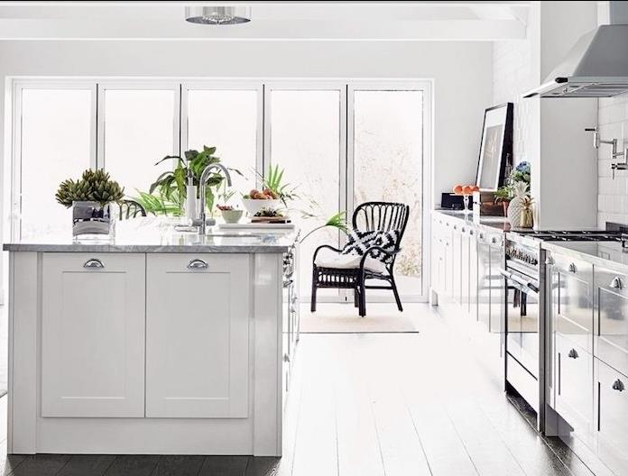 vitlackerat kök med möbler och vit centralö med bänkskiva i marmor, vitkalkat parkettgolv, klädda i vita kakel, inslag av gröna växter