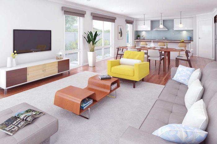 kuchyňa otvorená do obývačky, biela skrinka a modrý splashback, drevený stôl a stoličky, otvorenie obývačky so sedačkou a sivým kobercom, dizajnérsky konferenčný stolík, žlté kreslo, drevená televízna skrinka