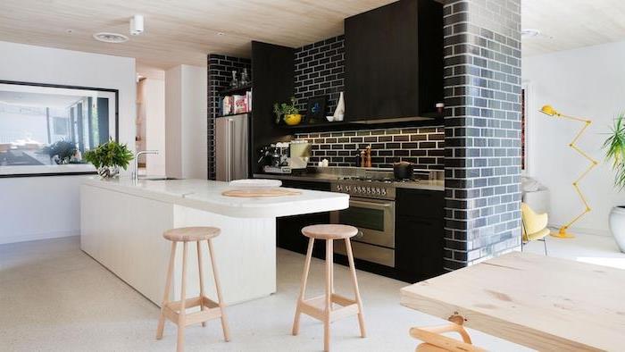 modernt vitt och svart kök, köksskåp och svart tegelvägg, vit centralö med träpallar, grått golv