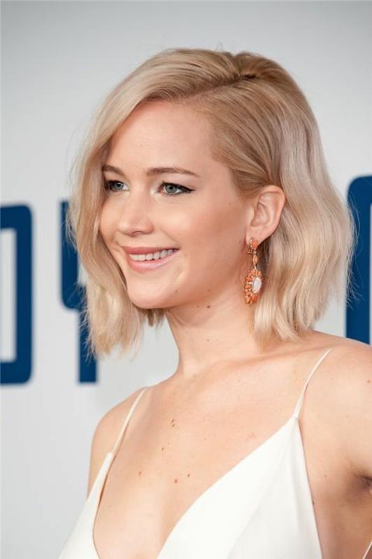detailný záber na Jennifer Lawrence, s vlnitou svetlou blondou s oddelenými bokmi, na sebe biely vrchný pásik a oranžové náušnice