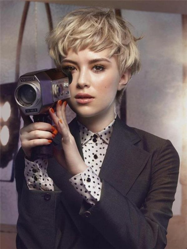 pixie strih, žena s veľmi krátkymi, strapatými a vrstvenými blond vlasmi, na sebe má košeľu a sako a retro fotoaparát