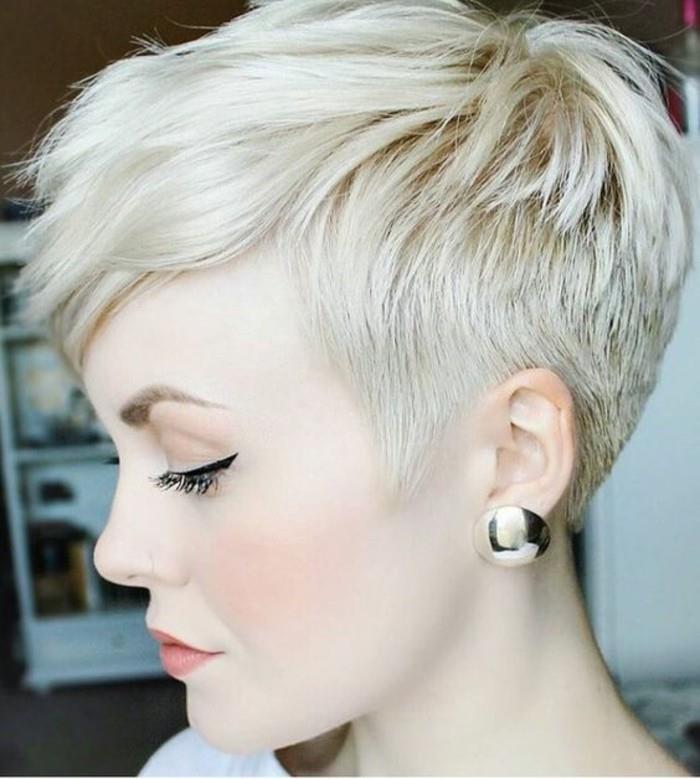 krátke zrážky, platinová blondínka v profile, vlasy ostrihané nakrátko po stranách a s dlhou ofinou, čierne očné linky a veľké zlaté náušnice