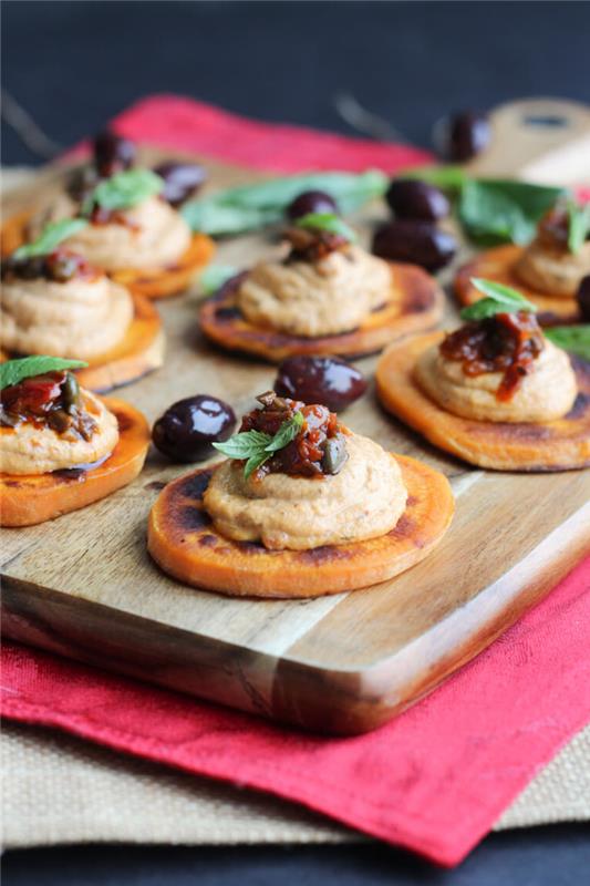 sötpotatisskivor, hummus och oliver på toppen, grönsaksrätt, arrangerade på en träbräda