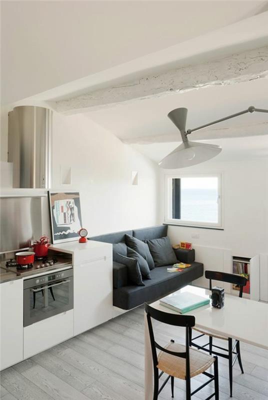 طبقات لغرف المعيشة الصغيرة ، ومساحة بيضاء مع أرضية صفائحية شاحبة ، وتحتوي على مطبخ صغير ، وكنبة رمادية داكنة مع وسائد متطابقة