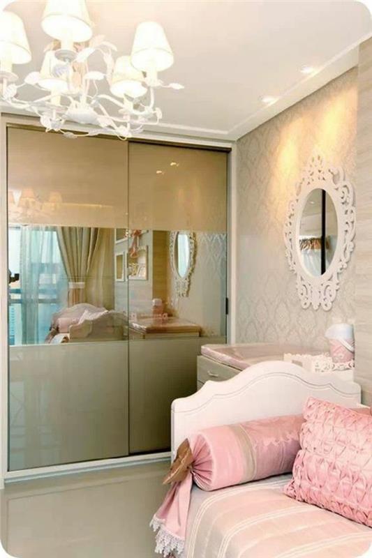 deco malá spálňa pre dospelých v romantickom štýle, s veľkým lustrom, bielym zrkadlom v barokovom štýle, šatníkom s posuvnými dverami v zlatej farbe, bielou posteľou s ružovým štvorcom a vankúšmi v tvare cukríka