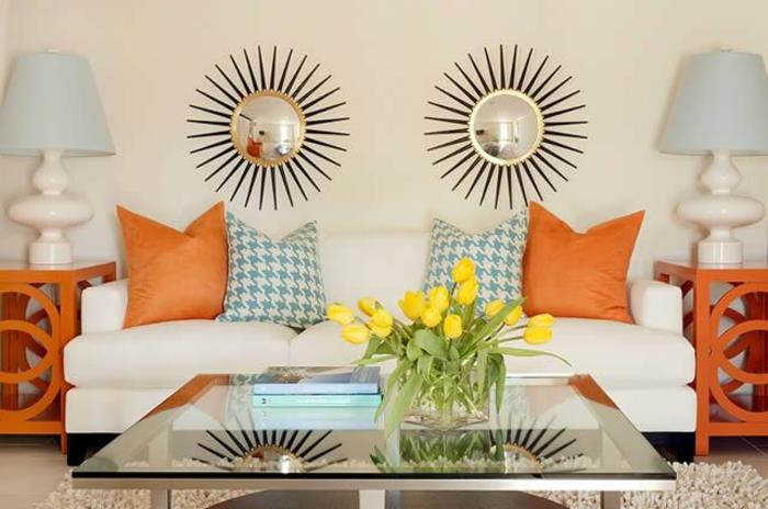 väggdekoration-med-dekorativ-spegel-vit-soffa-med-orange-blomma-kuddar-på-glas-bordet