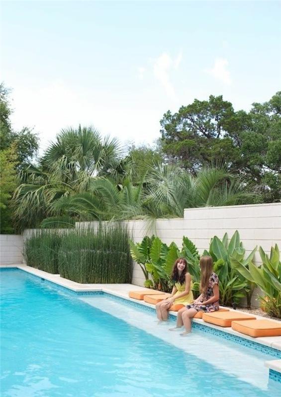 rozloženie vonkajšieho domu, nápady na výzdobu vonkajšej záhrady, obliecť drevenú vonkajšiu stenu z PVC v slonovinovej farbe, veľký bazén a oranžové štvorcové podložky okolo vody