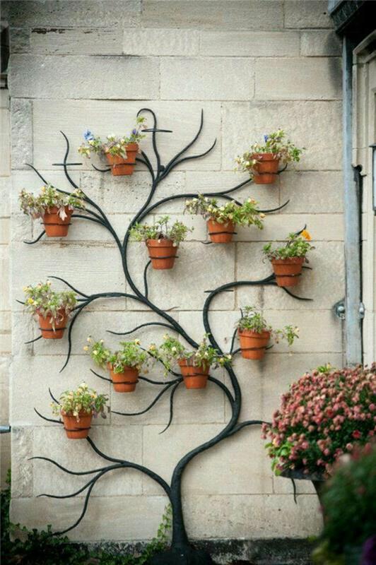 vonkajšia dispozícia domu, stena zdobená čiernym kovovým držiakom rastlín v tvare stromu, s konármi, na ktoré sme zavesili kvetináče s kvetmi