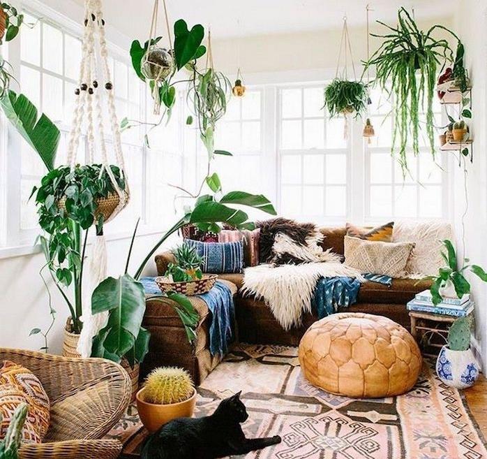 bohémske elegantné deo v obývačke, béžový puf, orientálny koberec, ratanové kreslo, hnedá rohová sedačka, orientálne vankúše, biele steny a závesné zelené rastliny