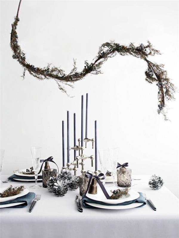 Skandinavisk nyårsdekoration, dekorativ gren ovanför ett bord med vit duk, ljushållare och silverkottar, vegetation decomönster