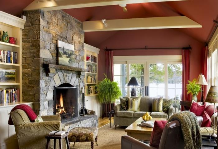 Rustikt vardagsrum med öppen spis i sten, röd vägg, soffor och fåtöljer, bokhylla, soffbord i trä, synlig balk