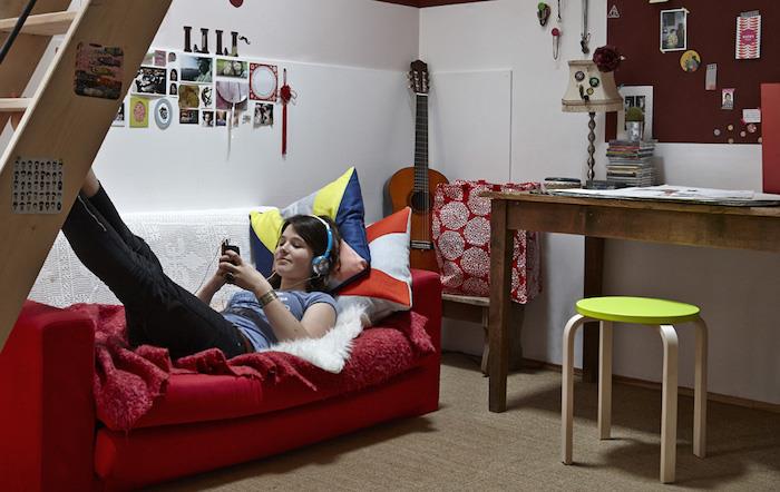 غرفة الفتاة المراهقة ، أريكة حمراء مغطاة بنقوش حمراء رقيق ، جدران بيضاء مزينة بإطارات صور