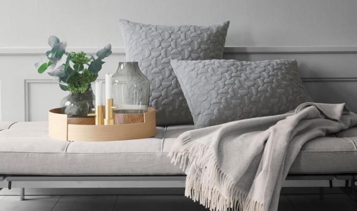 de viktiga tillbehören för ett skandinaviskt vardagsrum i hygge -deco, grå kuddar med texturerat mönster, en mysig filt och en vacker dekorativ träbricka med en liten keramisk vas