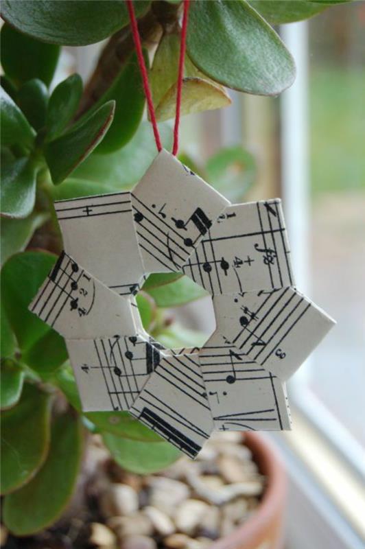 Vianočné DIY s hviezdou vytvorené s časťami hudobných partitúr a červenou niťou na zavesenie na rastlinu v dome alebo na vianočný stromček