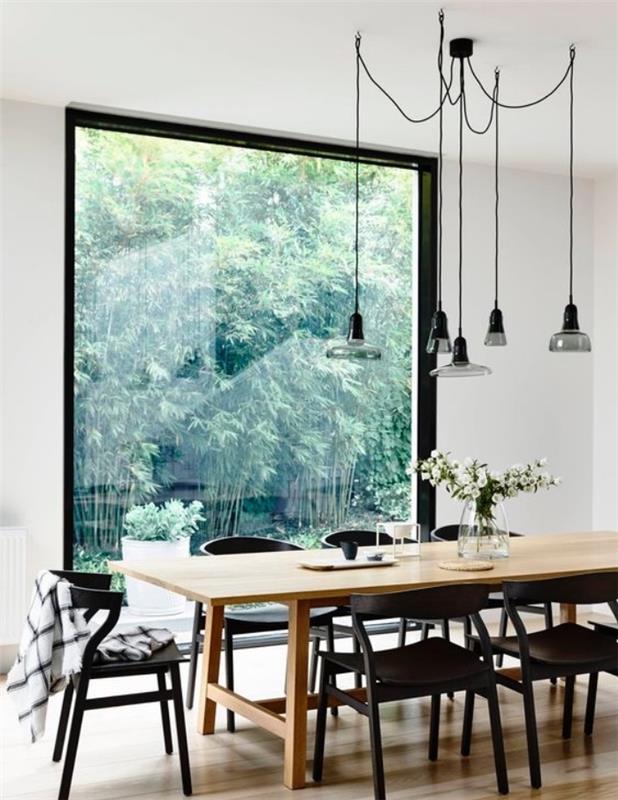 Škandinávska výzdoba jedálne so stolom z masívu, čiernymi stoličkami, priemyselnými závesnými svetlami, veľkým oknom