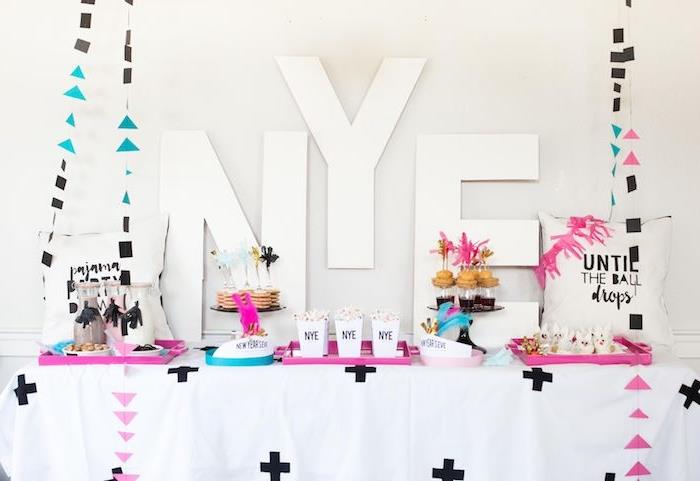 nyårsbokstäver i bakgrunden, bord med rosa och blå serveringsbrickor, geometriska figurer kransar, mini nyår godis pannkakor