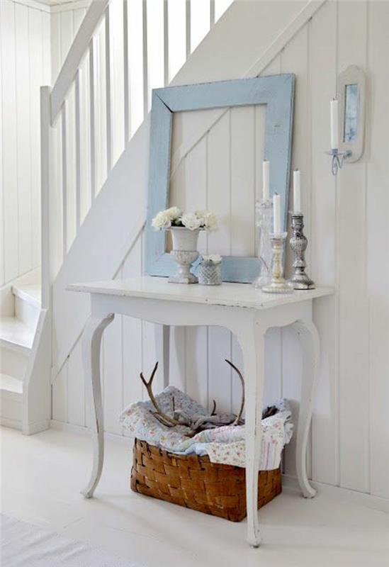 vstupná hala domu v pastelovo modrej a bielej farbe s rámom, ktorý slúži ako dekorácia na bielo namaľovaný stôl