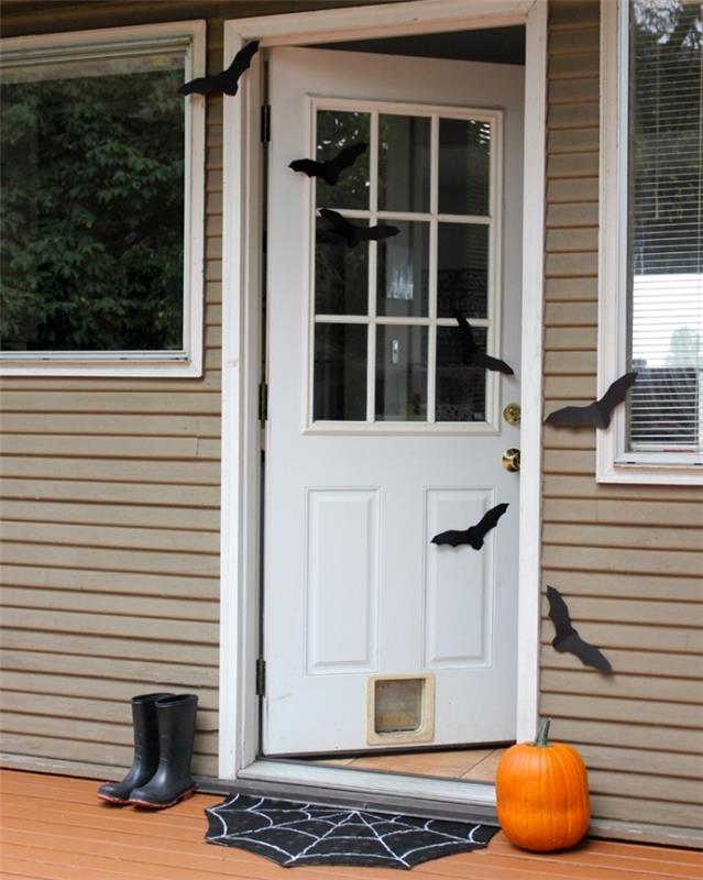 vit ytterdörr med enkel Halloween -dekoration i svarta pappersfladdermöss och orange pumpa
