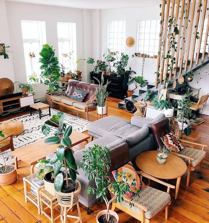 deko obývacia izba duch mestskej džungle s bohatou vegetáciou, sivá sedačka, nábytok a drevené podlahy a biele steny, mrežové schodisko