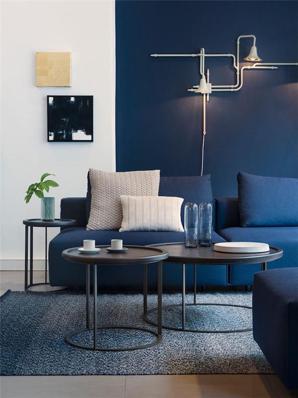 lägenhetsinredning, vit och blåmålad vägg, svart soffbord, mörkblå soffa, vit industrilampa