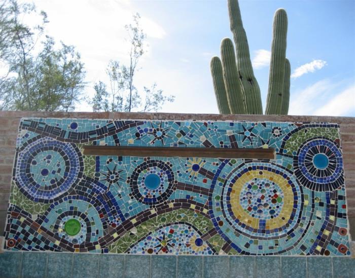 vonkajšia výzdoba steny v modrozelenej a žltej mozaike, veľký kaktus, ktorý sa týči nad mozaikou vložený na svetlo hnedú kamennú stenu