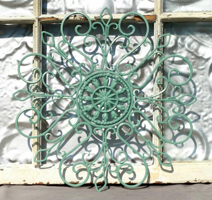 vonkajšie usporiadanie domu, mätový zelený kovový prvok, typ mandaly v retro štýle, umiestnený vedľa starého okenného rámu v opotrebovanej farbe slonovinovej kosti