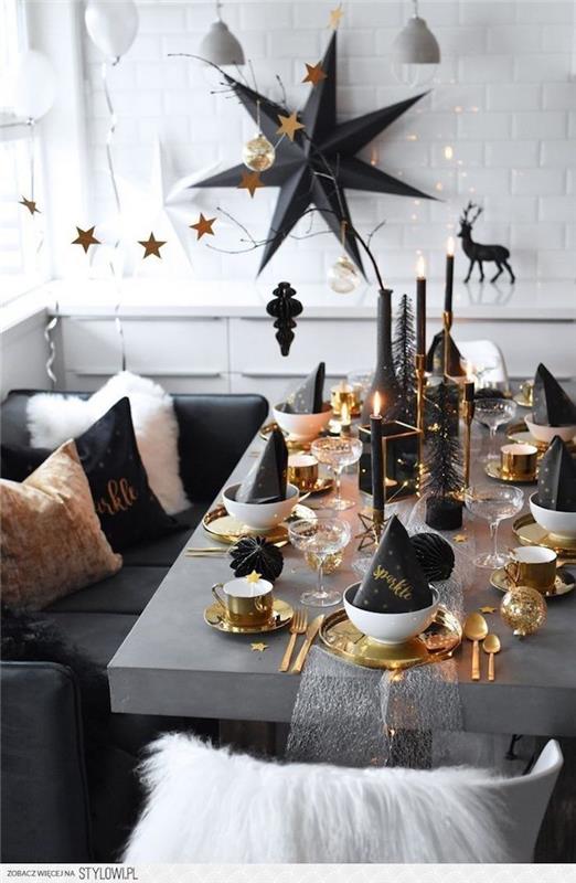 grått bord med guld- och vitt bestick och tallrikar, ljus och svarta dekor accenter ,, stor svart stjärna väggdekoration, snygg nyårsdekoration