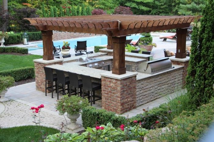 nápad, ako zariadiť záhradu s bazénom a krytou kuchyňou v masívnej drevenej streche a kamennom ostrove