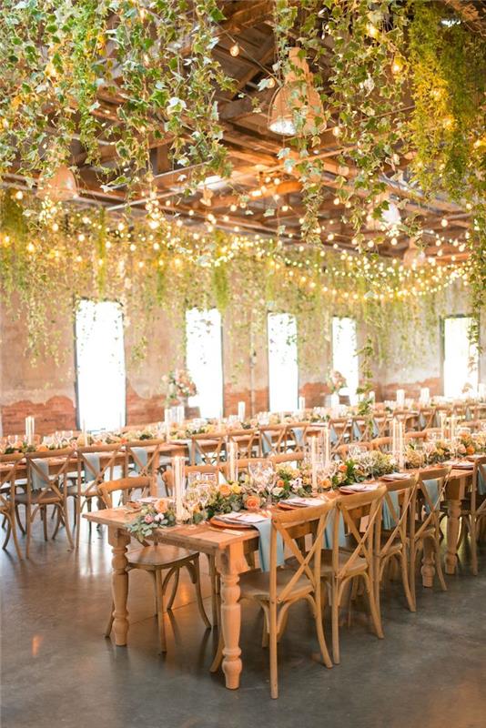 Nápad na výzdobu svadobného stropu s popínavou vegetáciou a svetlými girlandami nad stoličkami a stôl z vegetačného dreva, rustikálna svadobná téma v starých stodolách