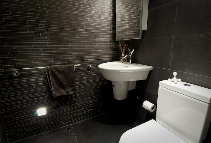حمام مصمم ، منشفة سوداء ، جدار رمادي غامق ، صنبور فولاذي ، وعاء مرحاض أبيض