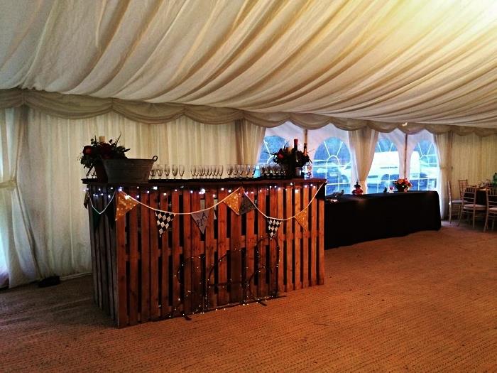 bröllopsmottagningsrum med barhörna i återvunnet trä dekorerat med en krans med vimplar, gör en drinkbar med pallar