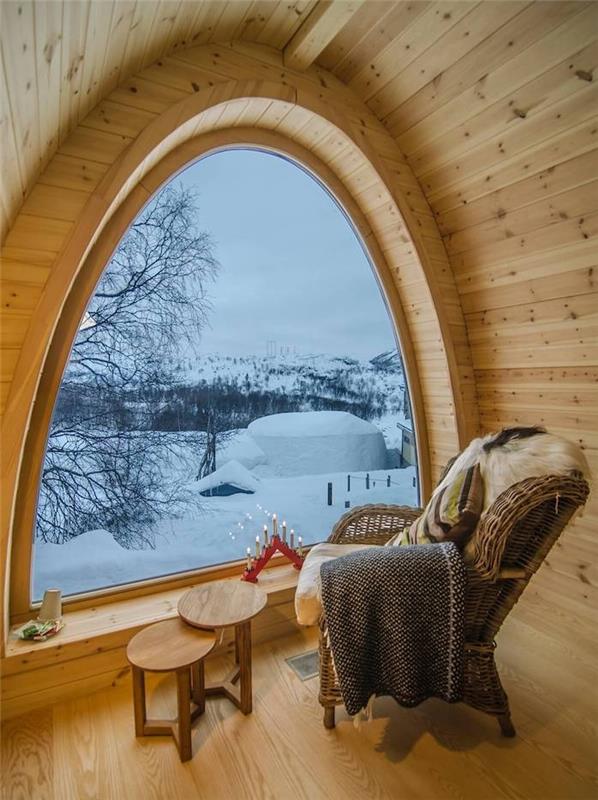 varm vardagsrumsinredning med vävda fåtölsbodade träbord och burspråk med utsikt över snöigt landskap