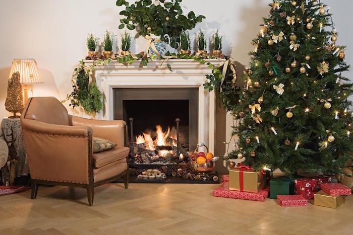 مدفأة في غرفة المعيشة على أرضية عائمة أو مشمع وكرسي بذراعين جلدي قديم وديكور عيد الميلاد مع شجرة عيد الميلاد وأشجار الصنوبر الصغيرة والعديد من النباتات الخضراء الشتوية
