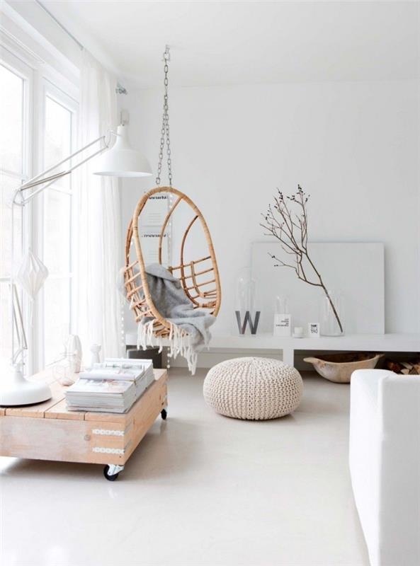 kokande vit interiör i ett rent vardagsrum i skandinavisk stil med en rottinggunga inomhus och en stickad puff