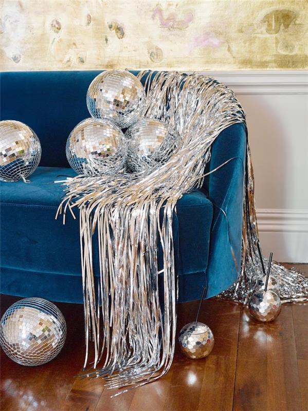 silverkrans och spegelbollar på en ankablå soffa i ett kokande vardagsrum inrett för nyårsdagen