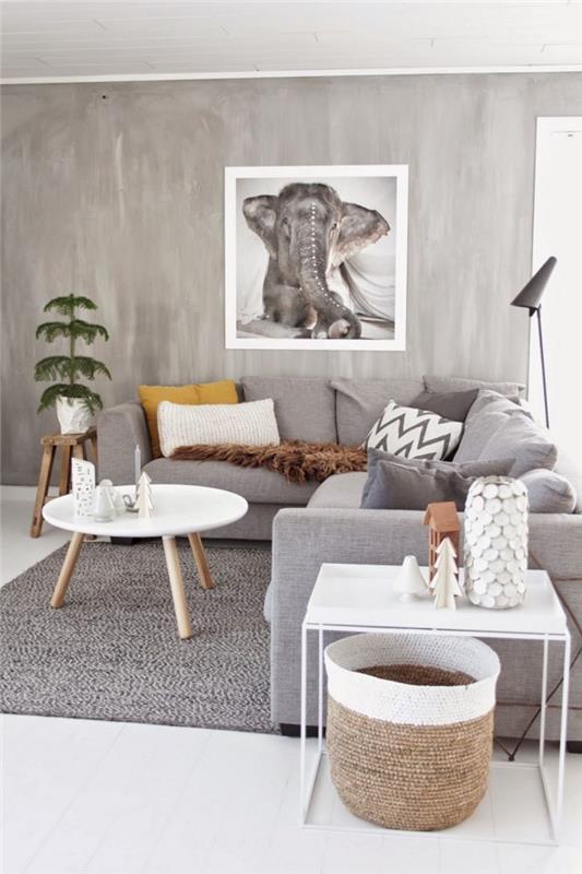 grå vardagsrumsinredning i modern skandinavisk stil med en stor grå hörnsoffa täckt med dekorativa kuddar i enfärgad eller med geometriska mönster och dekorativa accenter av naturligt trä, grå väggcementeffekt sublimerad av en stor fotoposter